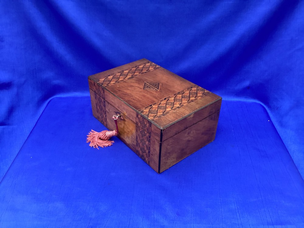 A rectangular Victorian walnut keepsake box featuring geometric parquetry inlay bands, a diamond escutcheon, and a key with a pink tassel. View VII