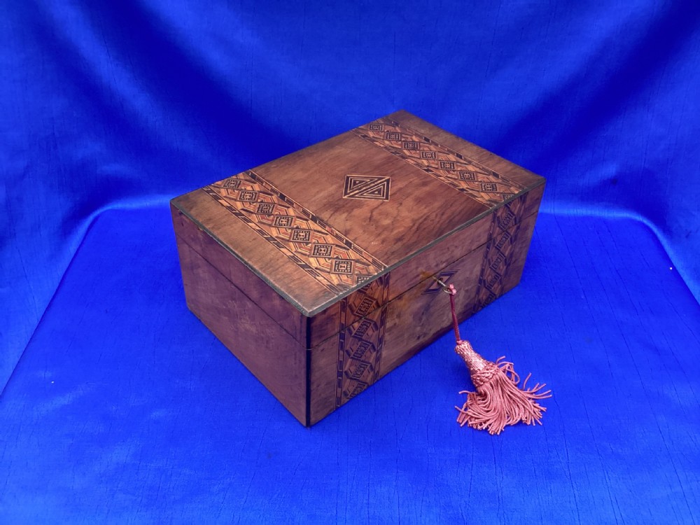 A rectangular Victorian walnut keepsake box featuring geometric parquetry inlay bands, a diamond escutcheon, and a key with a pink tassel. View VIII