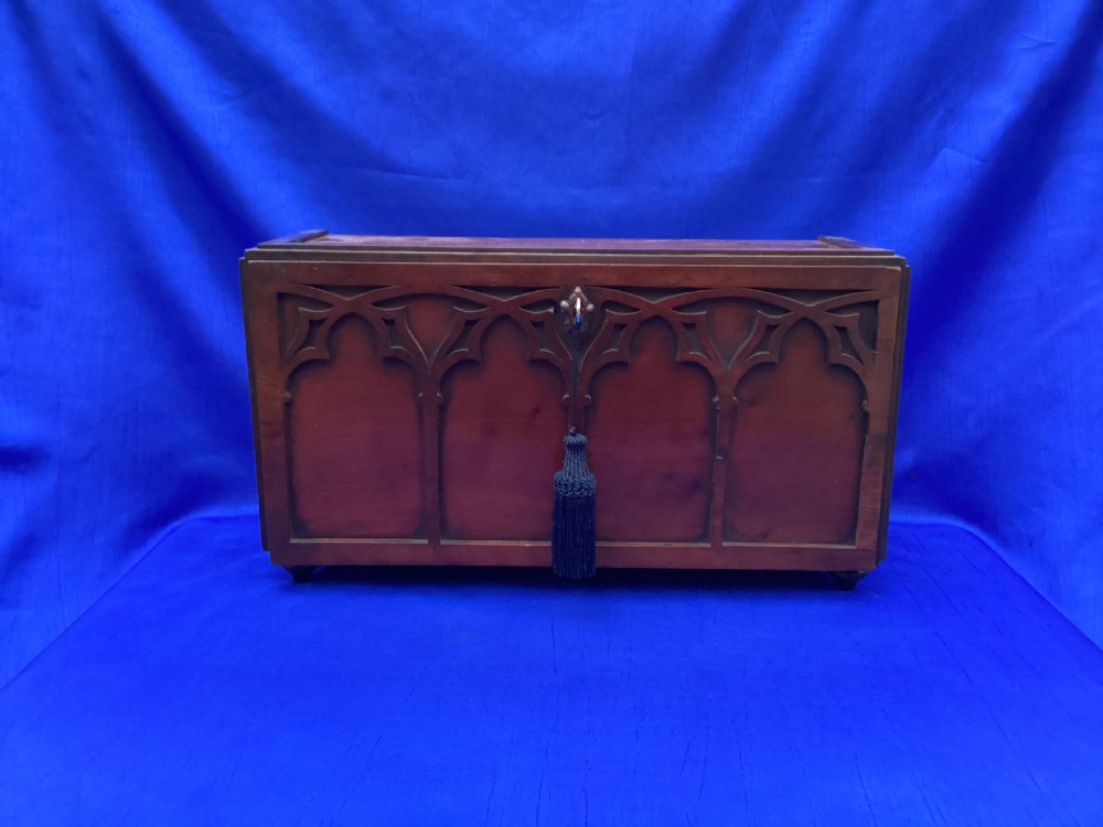 A rectangular mahogany table cabinet with carved Gothic blind tracery along the front face and a central keyhole with a black tassel attached.