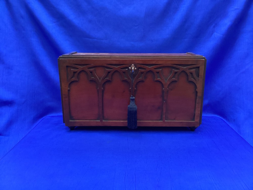 A rectangular mahogany table cabinet with carved Gothic blind tracery along the front face and a central keyhole with a black tassel attached. View II