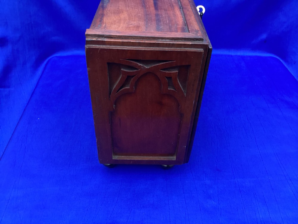 A rectangular mahogany table cabinet with carved Gothic blind tracery along the front face and a central keyhole with a black tassel attached. View III