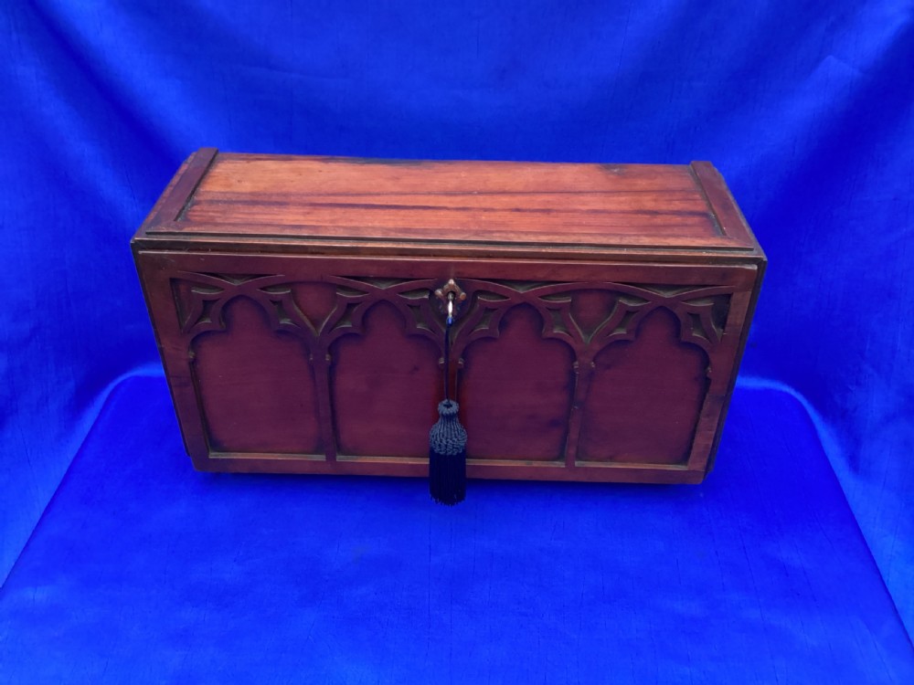 A rectangular mahogany table cabinet with carved Gothic blind tracery along the front face and a central keyhole with a black tassel attached. View IV