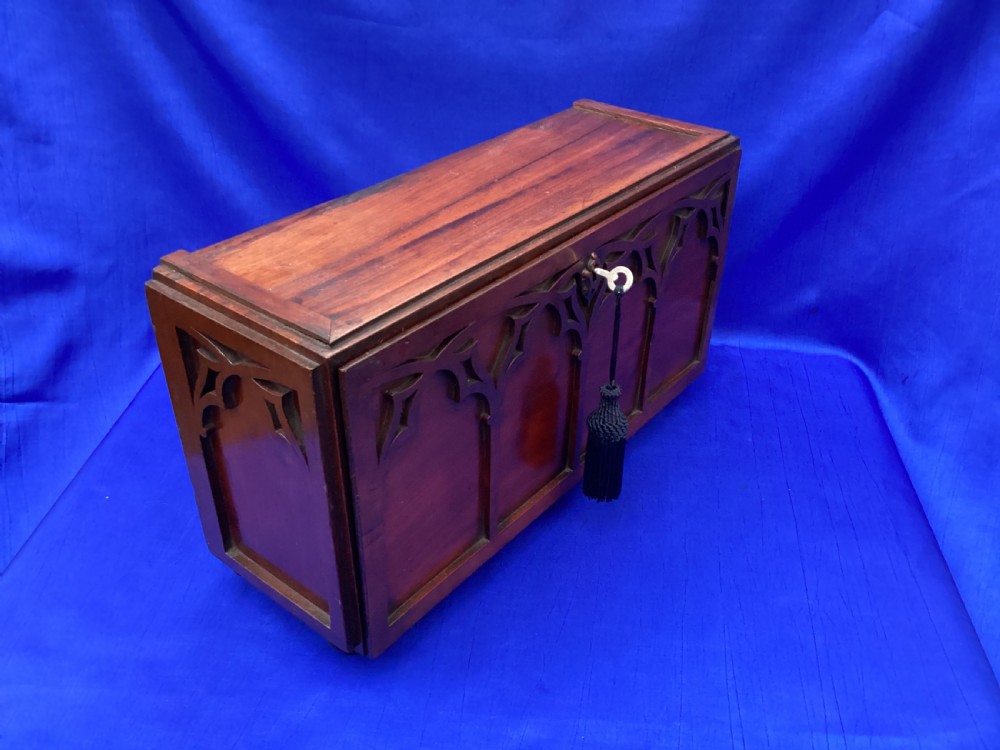 A rectangular mahogany table cabinet with carved Gothic blind tracery along the front face and a central keyhole with a black tassel attached. View VI