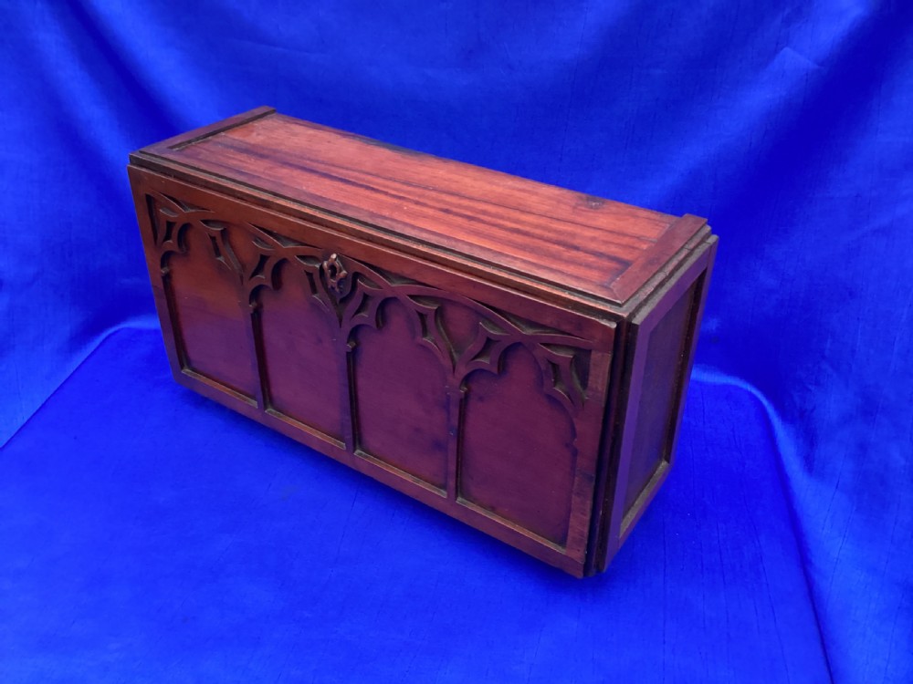 A rectangular mahogany table cabinet with carved Gothic blind tracery along the front face and a central keyhole with a black tassel attached. View VII