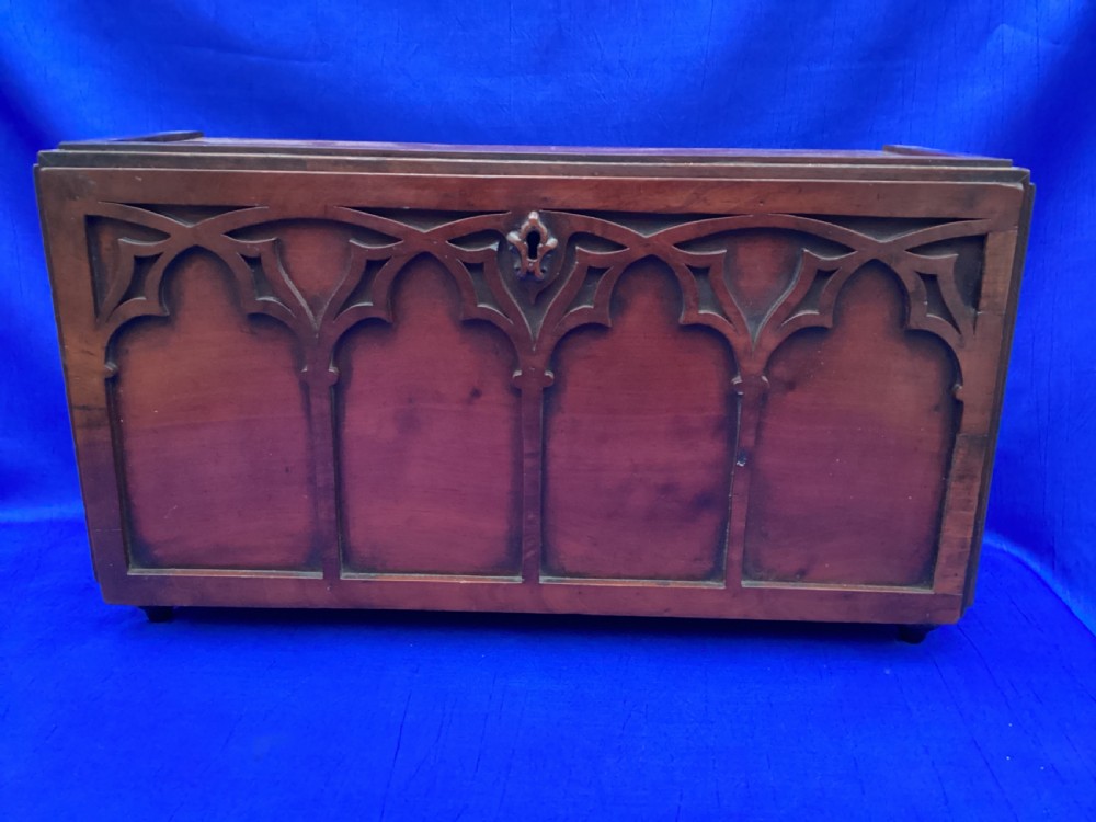 A rectangular mahogany table cabinet with carved Gothic blind tracery along the front face and a central keyhole with a black tassel attached. View VIII
