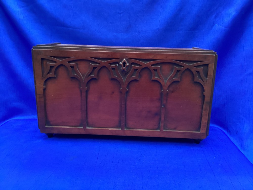 A rectangular mahogany table cabinet with carved Gothic blind tracery along the front face and a central keyhole with a black tassel attached. View IX