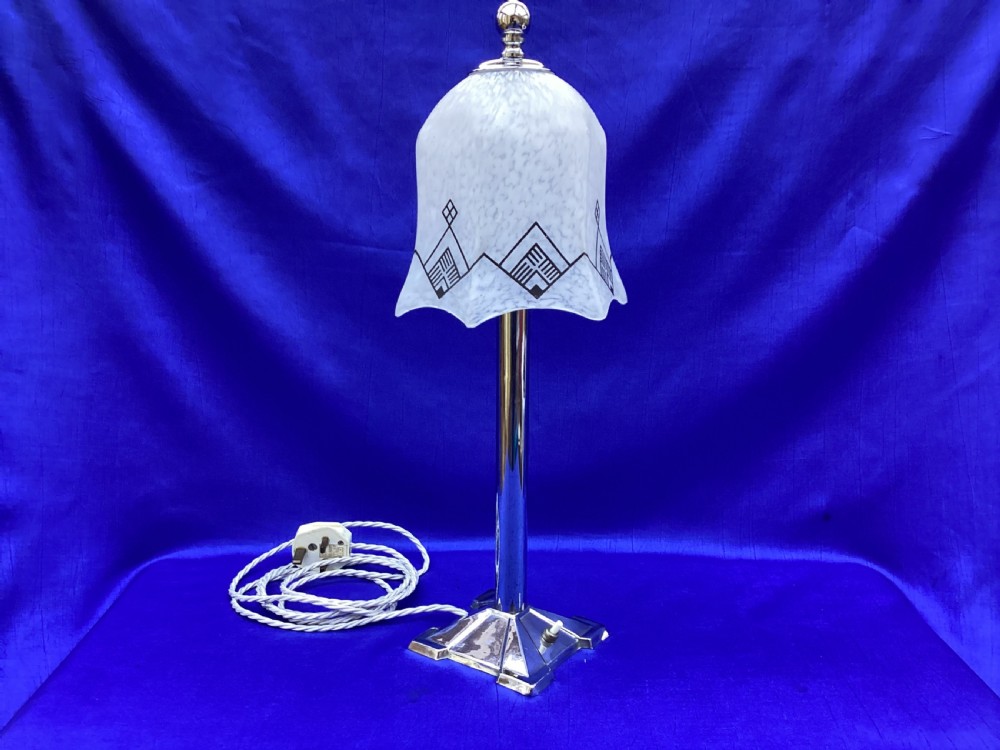 An Art Deco chrome table lamp featuring a central column stem, stepped square base, and a mottled frosted glass bell shade decorated with black geometric diamond motifs.