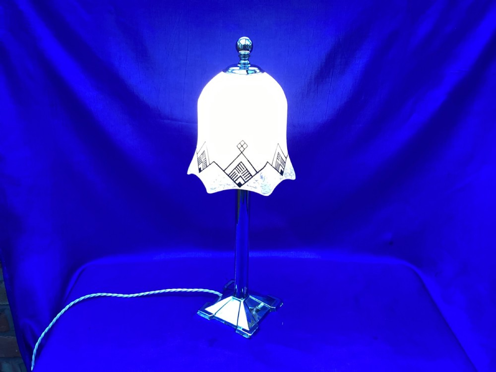 An Art Deco chrome table lamp featuring a central column stem, stepped square base, and a mottled frosted glass bell shade decorated with black geometric diamond motifs. View III