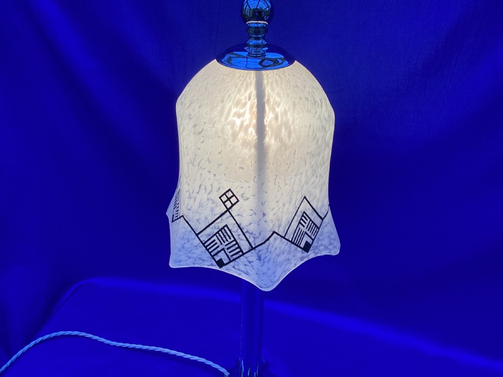 An Art Deco chrome table lamp featuring a central column stem, stepped square base, and a mottled frosted glass bell shade decorated with black geometric diamond motifs. View IV
