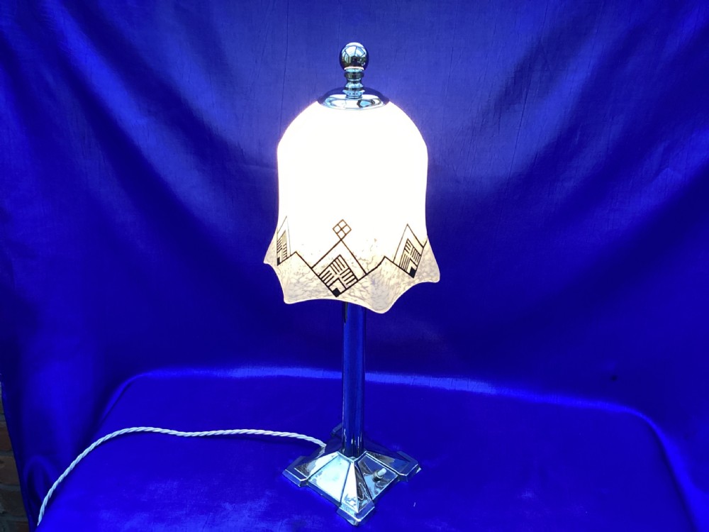 An Art Deco chrome table lamp featuring a central column stem, stepped square base, and a mottled frosted glass bell shade decorated with black geometric diamond motifs. View V