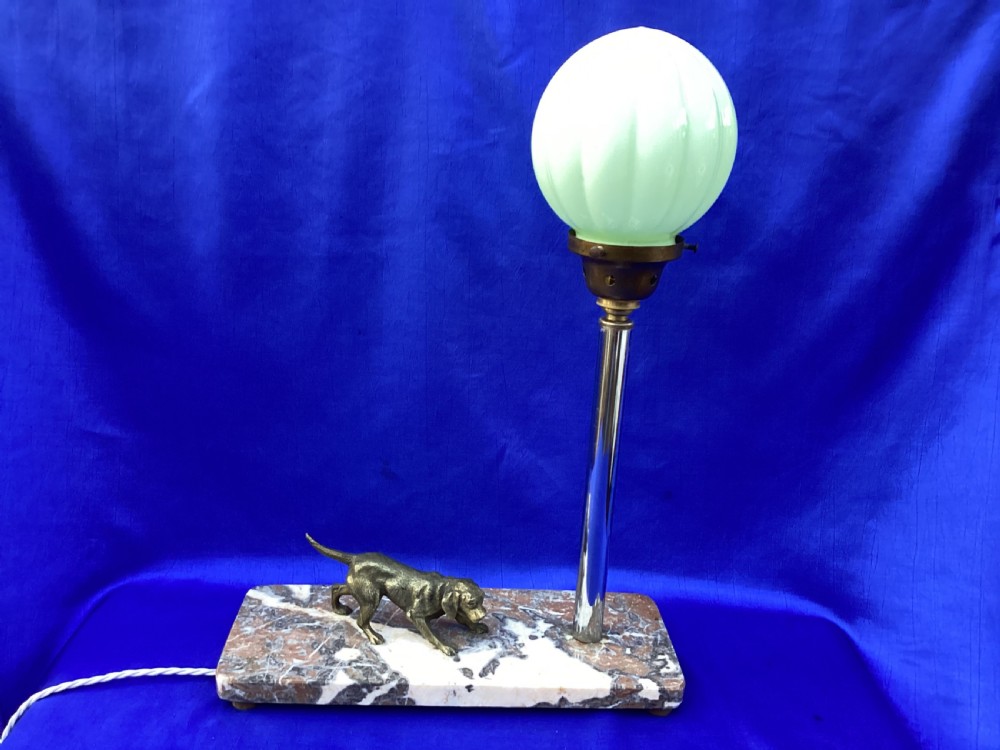An Art Deco French table lamp featuring a cast brass hound figure mounted on a rectangular veined marble base beside a stem supporting a pale green globe shade.