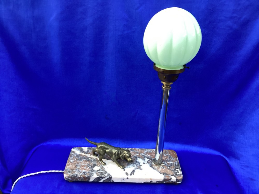 An Art Deco French table lamp featuring a cast brass hound figure mounted on a rectangular veined marble base beside a stem supporting a pale green globe shade. View VI