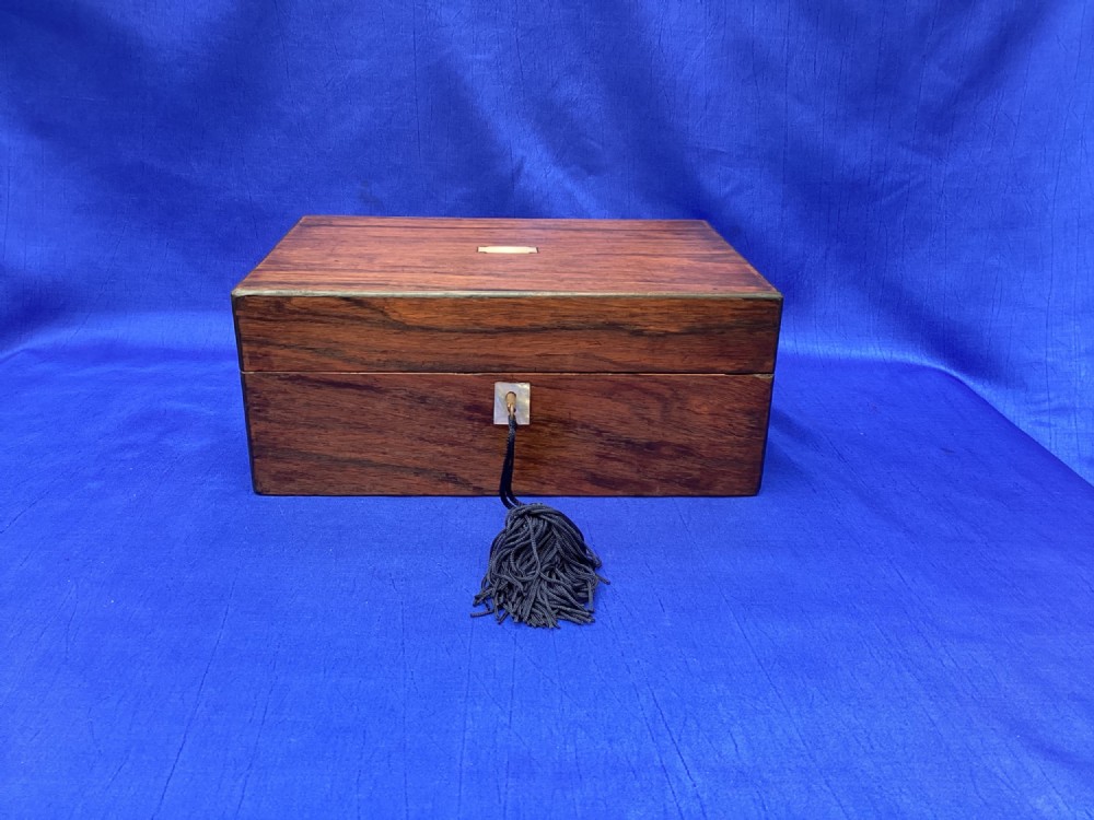 A rectangular dark rosewood trinket box with a mother-of-pearl cartouche on top, a mother-of-pearl keyhole escutcheon, and a brass key with a black tassel.