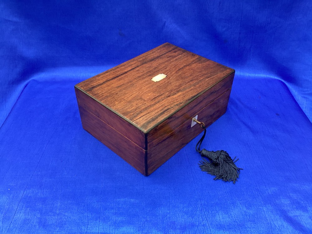 A rectangular dark rosewood trinket box with a mother-of-pearl cartouche on top, a mother-of-pearl keyhole escutcheon, and a brass key with a black tassel. View II
