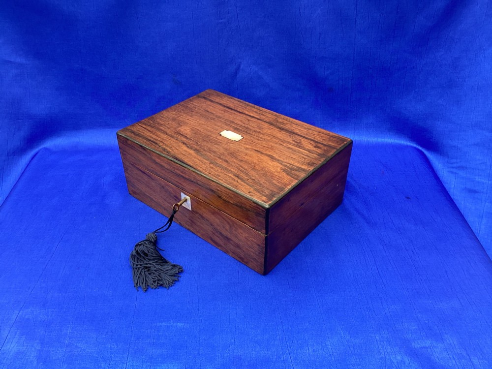 A rectangular dark rosewood trinket box with a mother-of-pearl cartouche on top, a mother-of-pearl keyhole escutcheon, and a brass key with a black tassel. View III