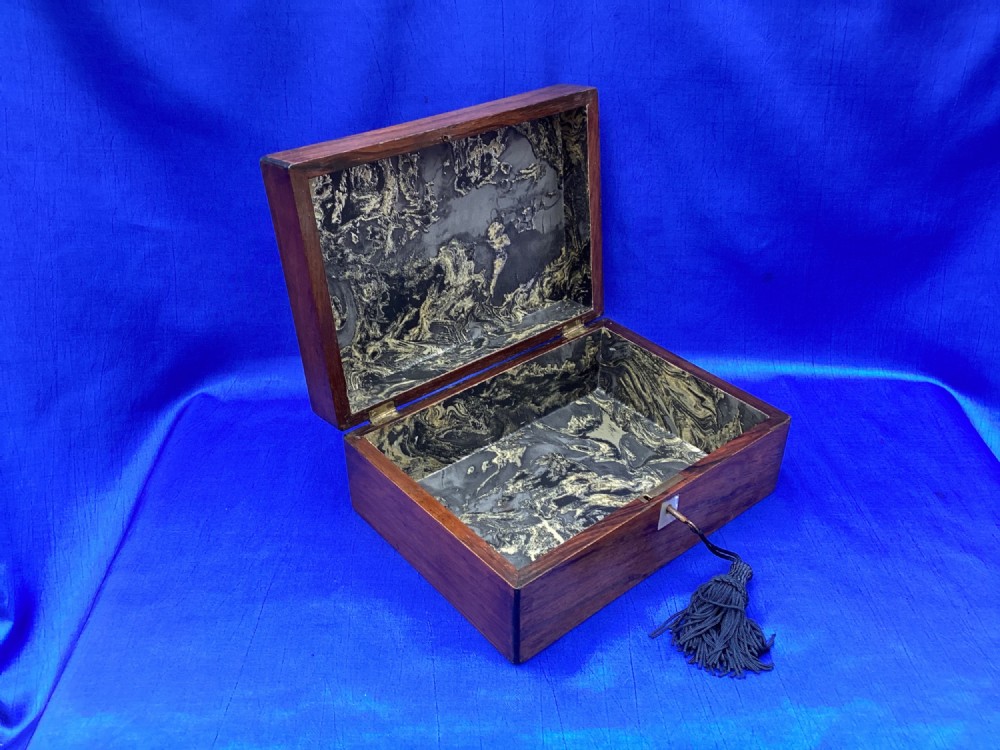 A rectangular dark rosewood trinket box with a mother-of-pearl cartouche on top, a mother-of-pearl keyhole escutcheon, and a brass key with a black tassel. View V