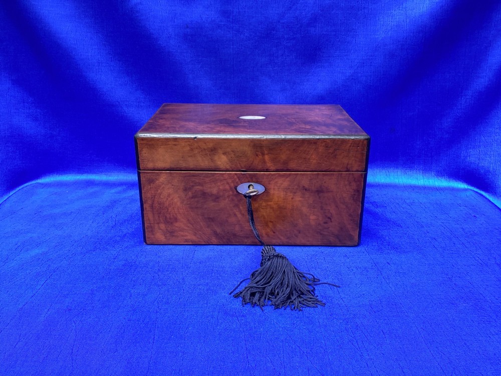 A rectangular Victorian mahogany box with a polished finish, a mother-of-pearl cartouche inlay on the lid, a keyhole escutcheon, and a brass key with a black tassel.