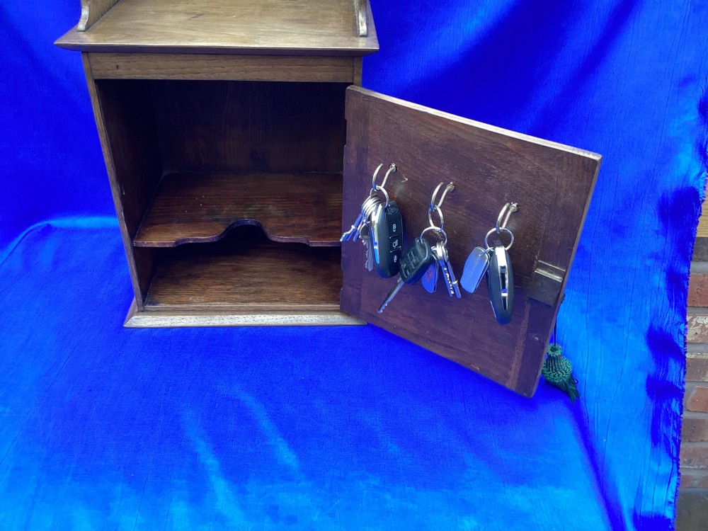 An Arts and Crafts medium brown oak key cabinet featuring an arched shaped gallery top and elaborate metal strap hinges on the single cupboard door. View VI