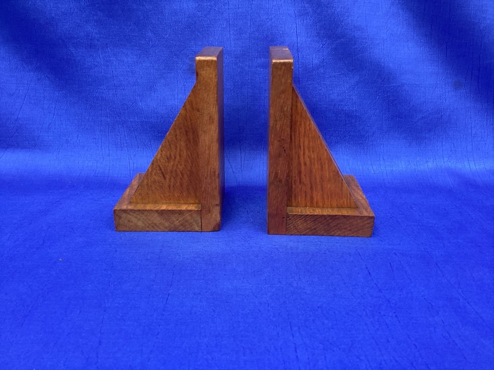 A pair of triangular solid oak wooden bookends featuring visible wood grain and a natural warm brown finish.