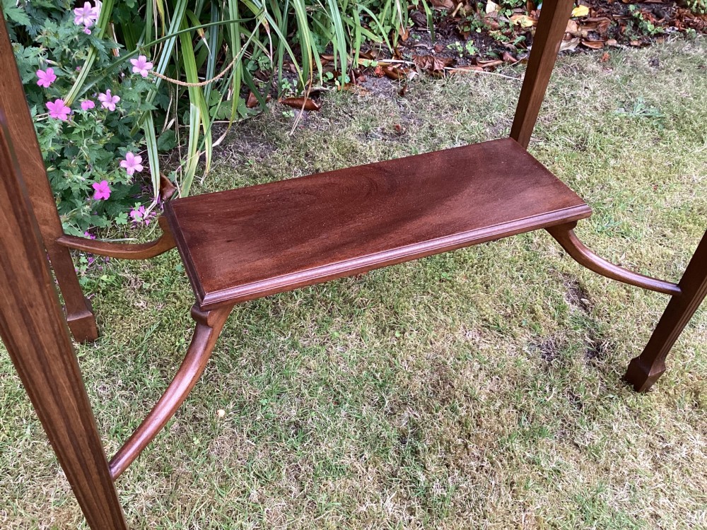An Edwardian mahogany fold-over games table featuring a carved floral frieze, fluted apron, slender tapered legs, and a lower tier shelf supported by swept stretchers. View III