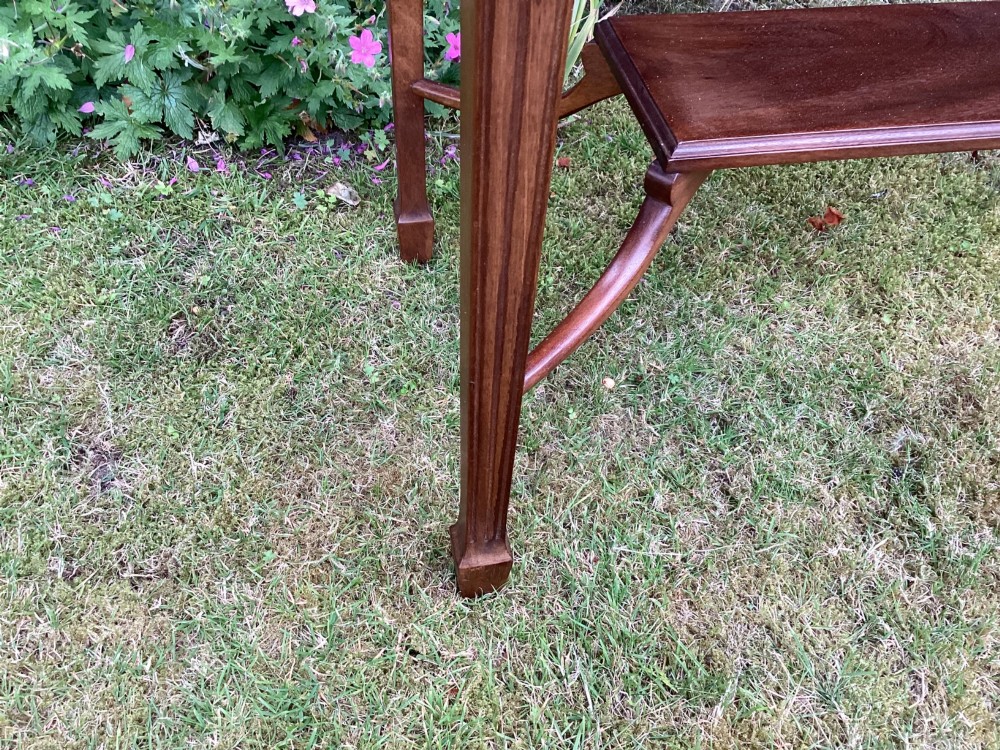 An Edwardian mahogany fold-over games table featuring a carved floral frieze, fluted apron, slender tapered legs, and a lower tier shelf supported by swept stretchers. View IV