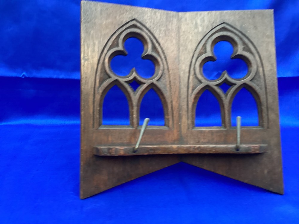 A dark carved oak desktop book stand featuring openwork Gothic lancet arches and trefoil tracery with brass page clips.
