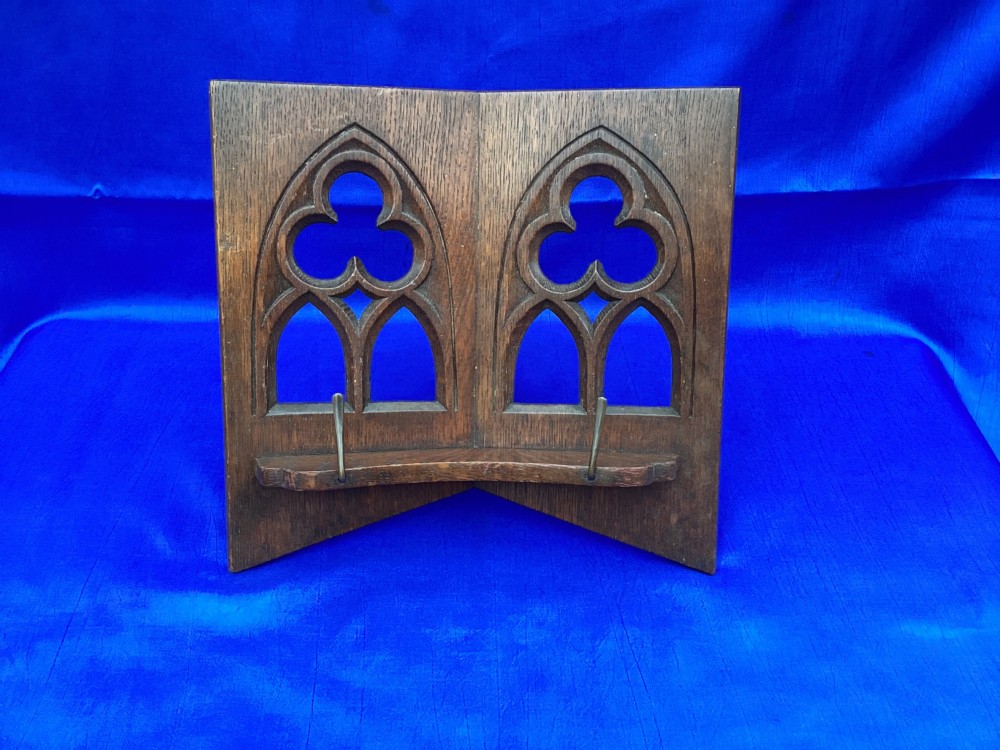A dark carved oak desktop book stand featuring openwork Gothic lancet arches and trefoil tracery with brass page clips. View V