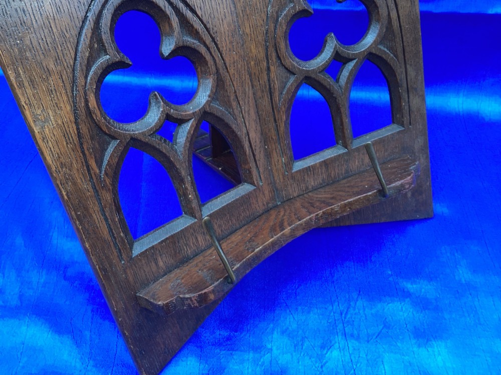 A dark carved oak desktop book stand featuring openwork Gothic lancet arches and trefoil tracery with brass page clips. View VI