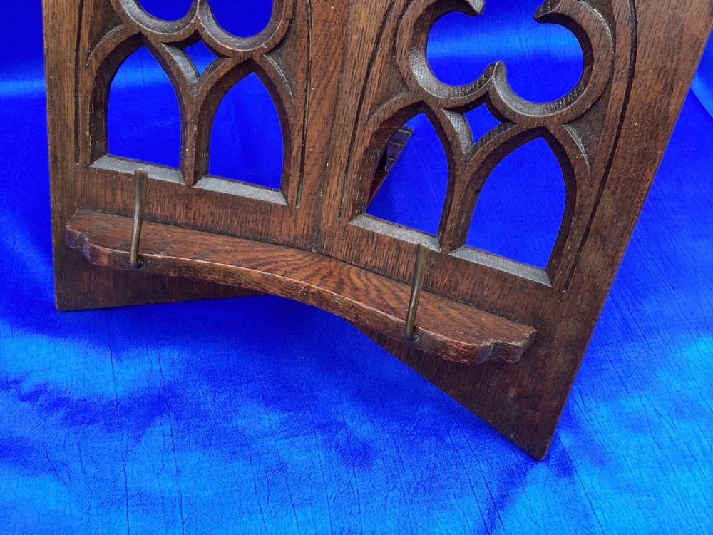 A dark carved oak desktop book stand featuring openwork Gothic lancet arches and trefoil tracery with brass page clips. View VII
