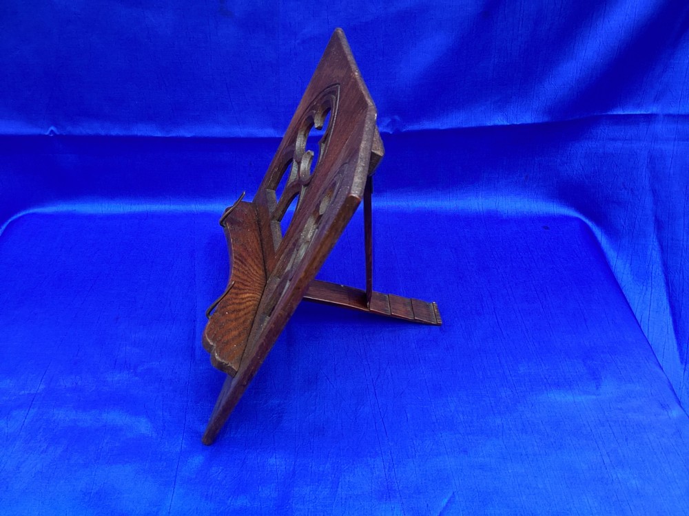 A dark carved oak desktop book stand featuring openwork Gothic lancet arches and trefoil tracery with brass page clips. View VIII