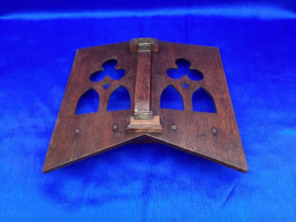 A dark carved oak desktop book stand featuring openwork Gothic lancet arches and trefoil tracery with brass page clips. View IX