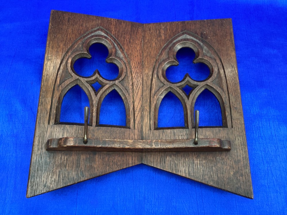 A dark carved oak desktop book stand featuring openwork Gothic lancet arches and trefoil tracery with brass page clips. View X