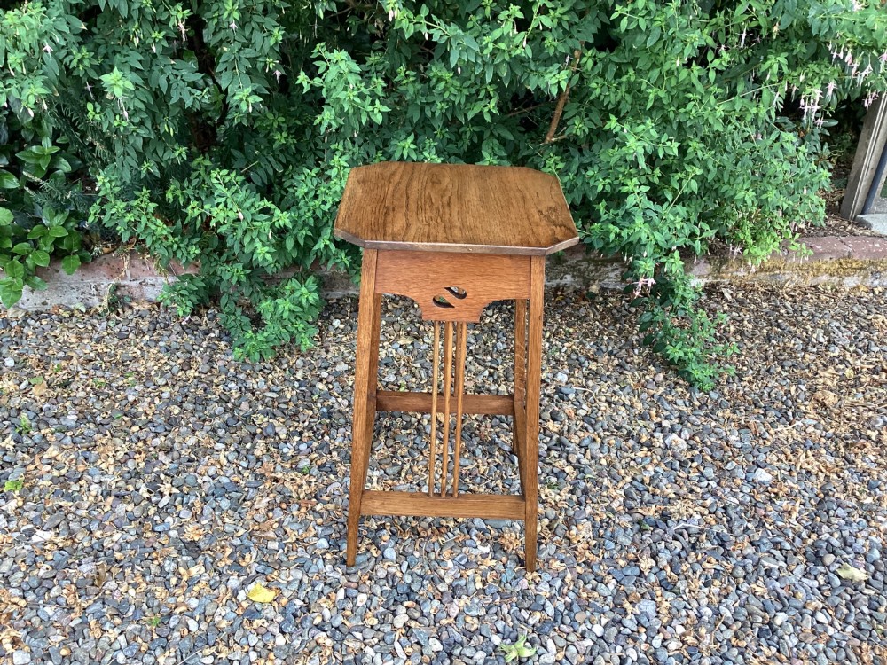 An Arts and Crafts solid oak plant table featuring an octagonal top, pierced cutout side aprons, central vertical slatted supports, and splayed legs with stretchers. View IV