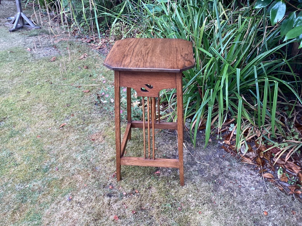 An Arts and Crafts solid oak plant table featuring an octagonal top, pierced cutout side aprons, central vertical slatted supports, and splayed legs with stretchers. View V