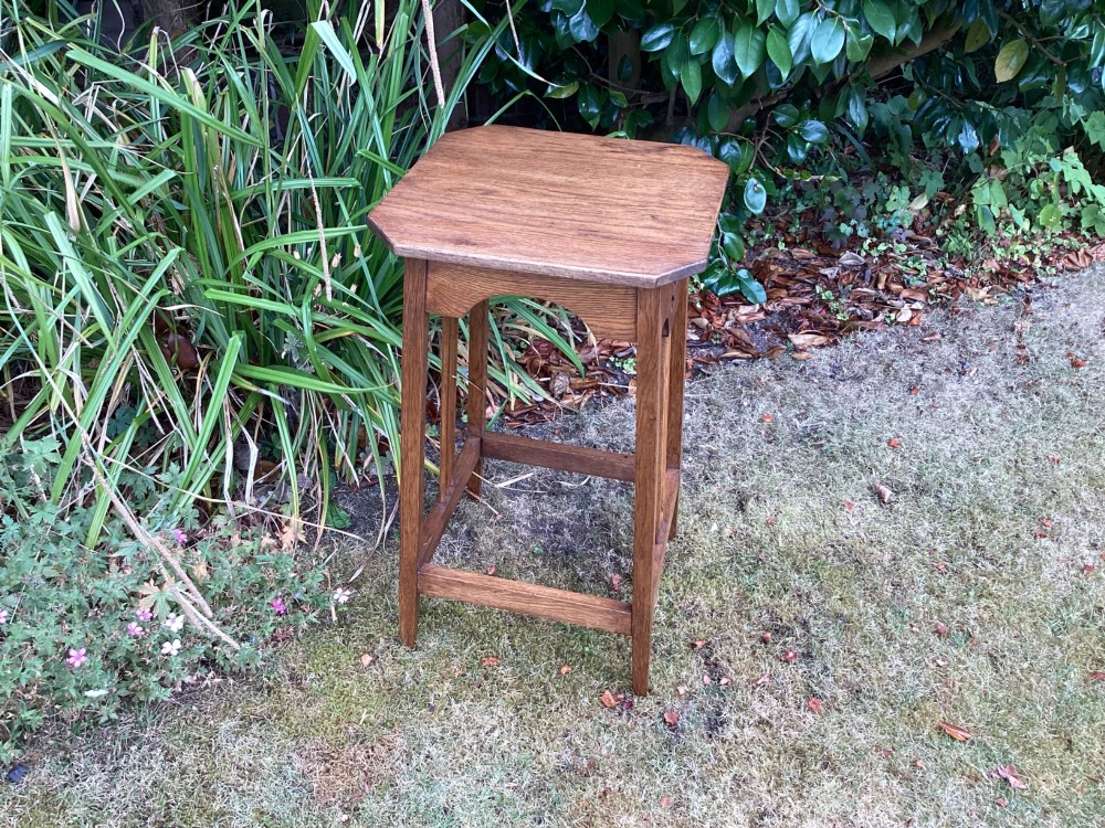 An Arts and Crafts solid oak plant table featuring an octagonal top, pierced cutout side aprons, central vertical slatted supports, and splayed legs with stretchers. View VI