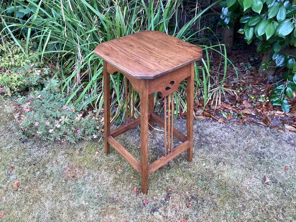 An Arts and Crafts solid oak plant table featuring an octagonal top, pierced cutout side aprons, central vertical slatted supports, and splayed legs with stretchers. View VII