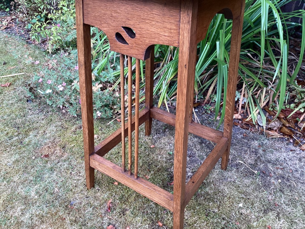 An Arts and Crafts solid oak plant table featuring an octagonal top, pierced cutout side aprons, central vertical slatted supports, and splayed legs with stretchers. View IX