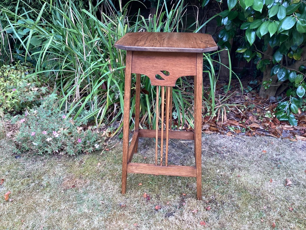 An Arts and Crafts solid oak plant table featuring an octagonal top, pierced cutout side aprons, central vertical slatted supports, and splayed legs with stretchers. View X