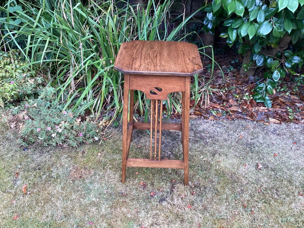 An Arts and Crafts solid oak plant table featuring an octagonal top, pierced cutout side aprons, central vertical slatted supports, and splayed legs with stretchers. View XI