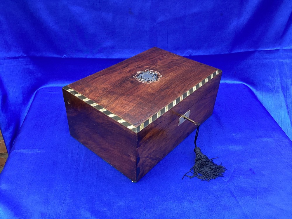 A rectangular Victorian mahogany box featuring decorative geometric inlay borders, a central crest motif on the lid, and a brass keyhole with a key and black tassel. View II