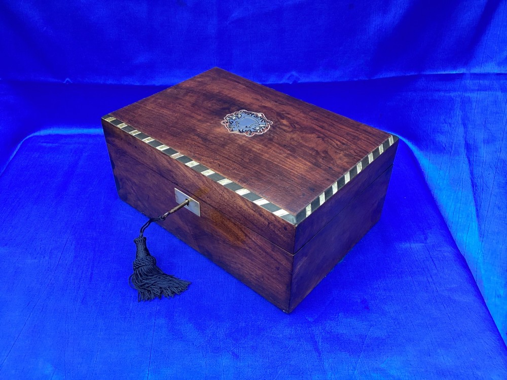 A rectangular Victorian mahogany box featuring decorative geometric inlay borders, a central crest motif on the lid, and a brass keyhole with a key and black tassel. View III