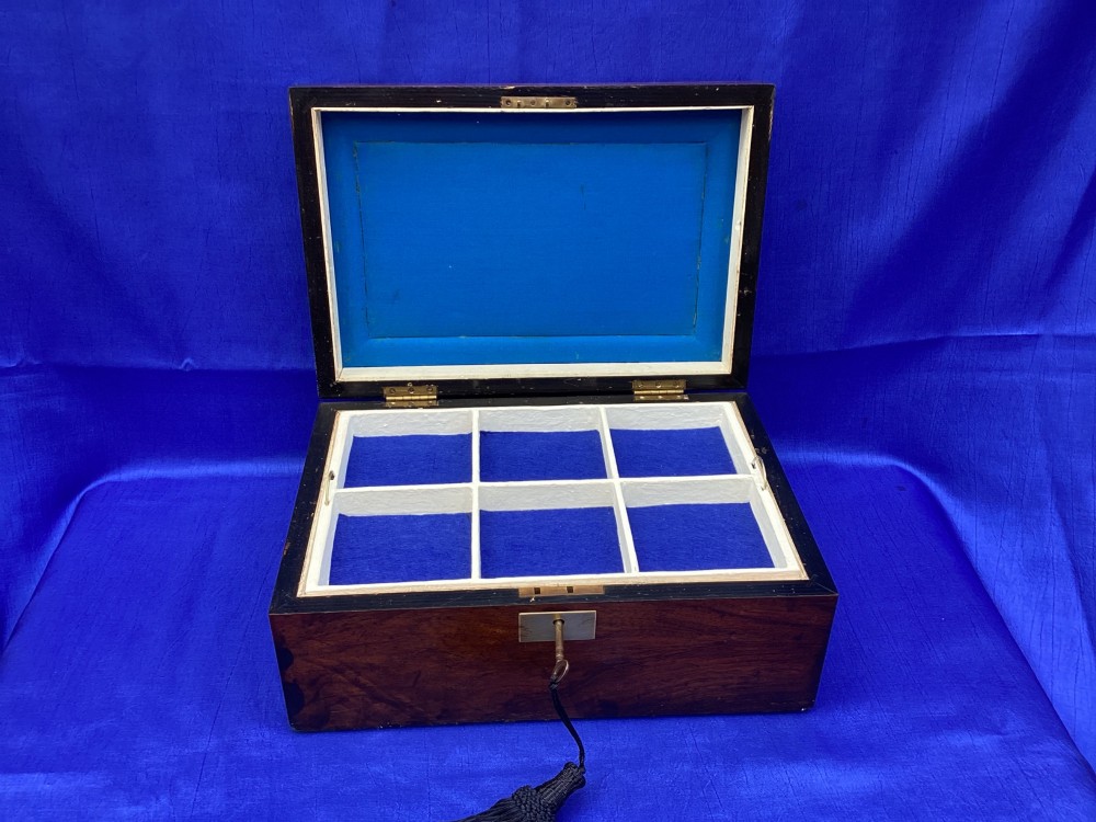 A rectangular Victorian mahogany box featuring decorative geometric inlay borders, a central crest motif on the lid, and a brass keyhole with a key and black tassel. View IV