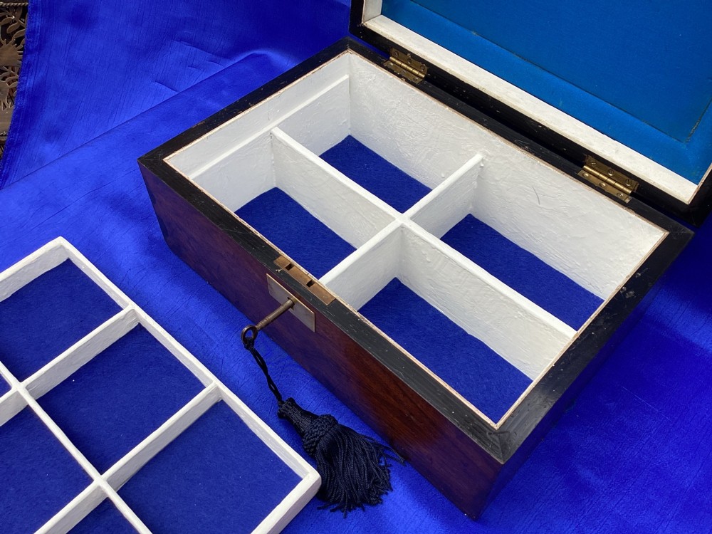 A rectangular Victorian mahogany box featuring decorative geometric inlay borders, a central crest motif on the lid, and a brass keyhole with a key and black tassel. View V