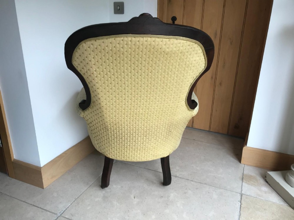 A Victorian mahogany parlour armchair featuring button-tufted pale yellow patterned upholstery, carved scroll arms, and turned front legs on castors. View II