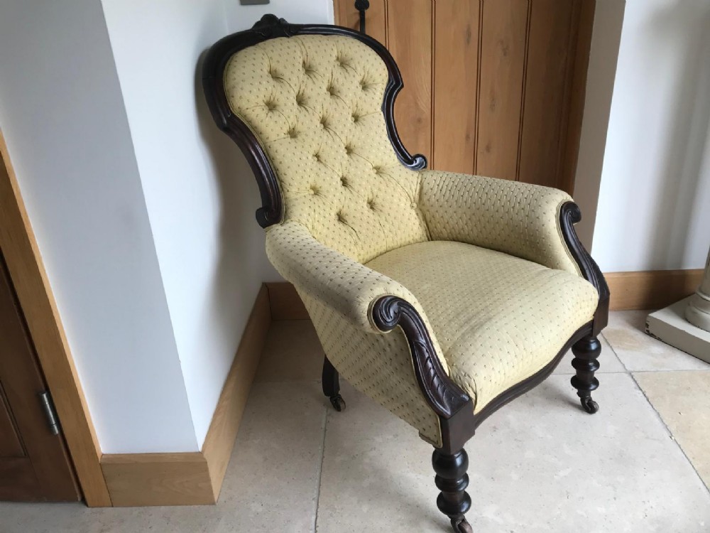 A Victorian mahogany parlour armchair featuring button-tufted pale yellow patterned upholstery, carved scroll arms, and turned front legs on castors. View VIII