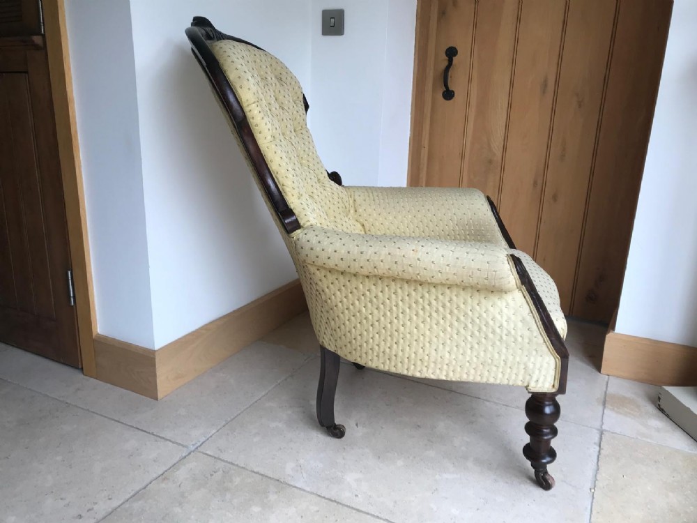 A Victorian mahogany parlour armchair featuring button-tufted pale yellow patterned upholstery, carved scroll arms, and turned front legs on castors. View IX