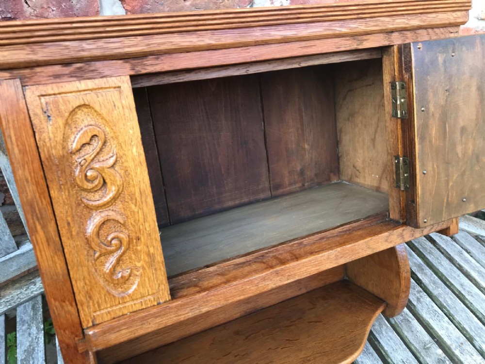 A Victorian carved oak wall cupboard featuring a central relief-carved door with bird motifs, flanked by scrolled side panels, a brass drop ring handle, and an open lower shelf. View II