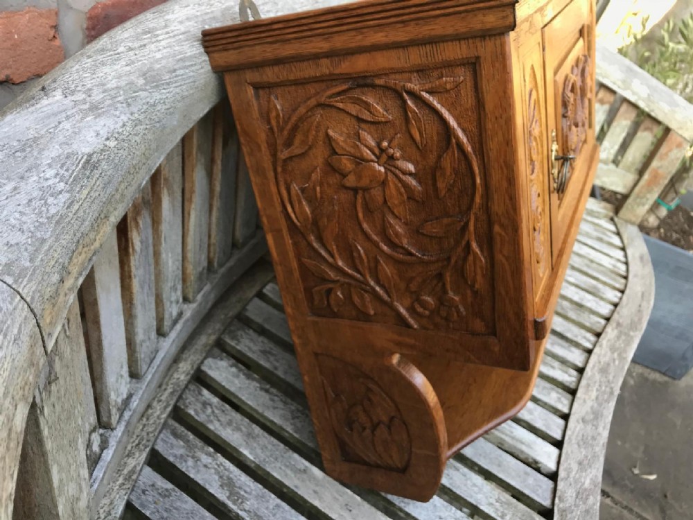 A Victorian carved oak wall cupboard featuring a central relief-carved door with bird motifs, flanked by scrolled side panels, a brass drop ring handle, and an open lower shelf. View V