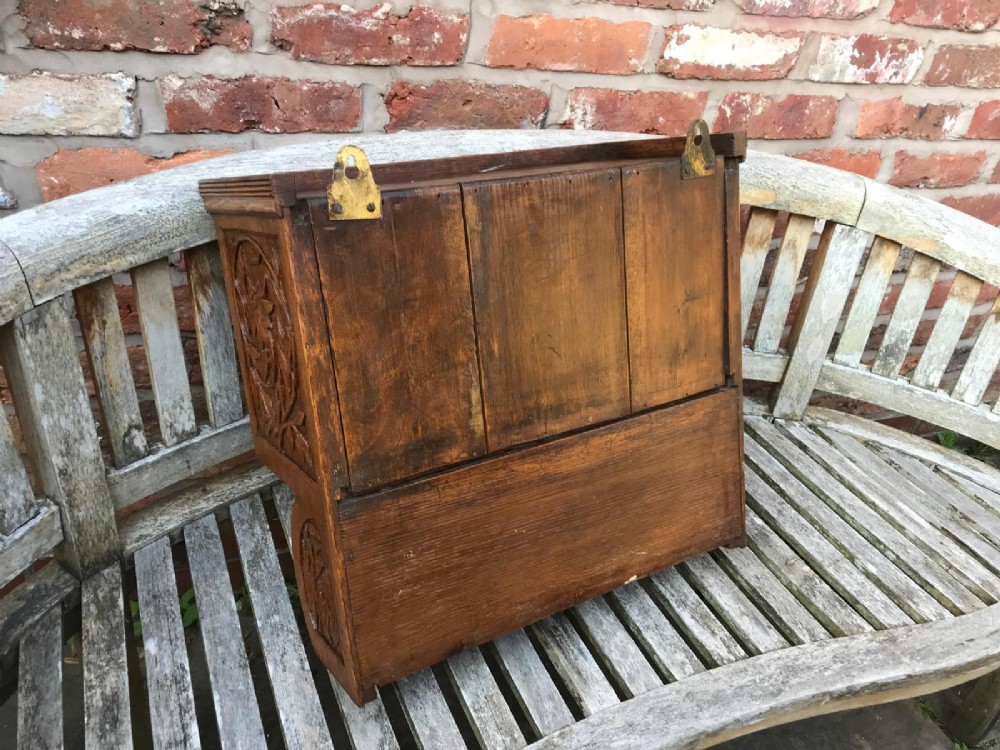 A Victorian carved oak wall cupboard featuring a central relief-carved door with bird motifs, flanked by scrolled side panels, a brass drop ring handle, and an open lower shelf. View VI