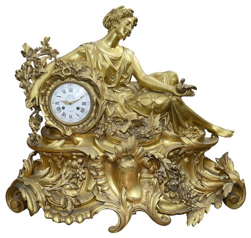 fig 1. A nineteenth-century gilt bronze clock garniture set comprising a central reclining classical female figure beside a clock dial flanked by two multi-arm candelabra.